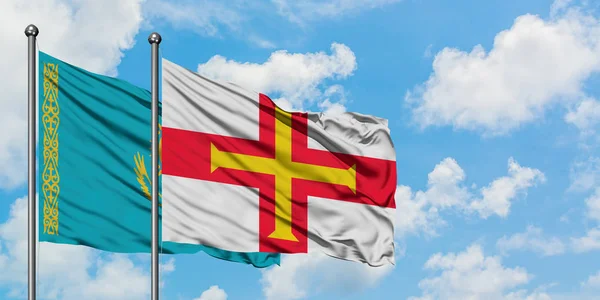 Bandera de Kazajstán y Guernsey ondeando en el viento contra el cielo azul nublado blanco juntos. Concepto diplomático, relaciones internacionales . — Foto de Stock