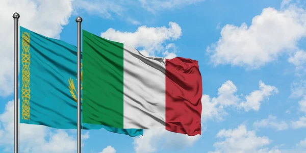 Bandera de Kazajstán e Italia ondeando en el viento contra el cielo azul nublado blanco juntos. Concepto diplomático, relaciones internacionales . — Foto de Stock