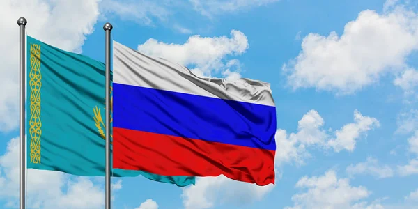 Cazaquistão e a bandeira da Rússia agitando no vento contra o céu azul nublado branco juntos. Conceito de diplomacia, relações internacionais . — Fotografia de Stock