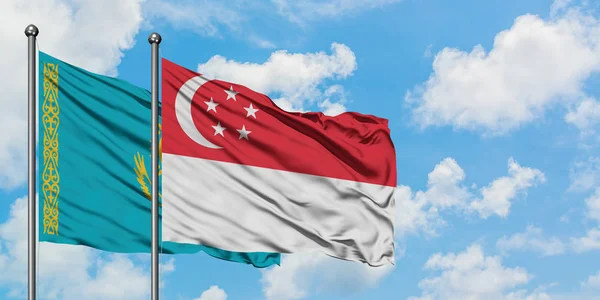 Cazaquistão e Singapura acenando com o vento contra o céu azul nublado branco juntos. Conceito de diplomacia, relações internacionais . — Fotografia de Stock