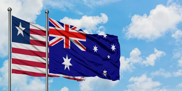 Bandera de Liberia y Australia ondeando en el viento contra el cielo azul nublado blanco juntos. Concepto diplomático, relaciones internacionales . — Foto de Stock