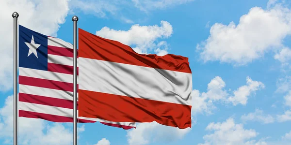 Bandera de Liberia y Austria ondeando en el viento contra el cielo azul nublado blanco juntos. Concepto diplomático, relaciones internacionales . — Foto de Stock