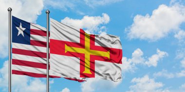 Liberya ve Guernsey bayrağı birlikte beyaz bulutlu mavi gökyüzüne karşı rüzgarda sallayarak. Diplomasi kavramı, uluslararası ilişkiler.