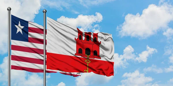 Liberia i flaga Gibraltaru machając w wiatr przed białym zachmurzone błękitne niebo razem. Koncepcja dyplomacji, stosunki międzynarodowe. — Zdjęcie stockowe