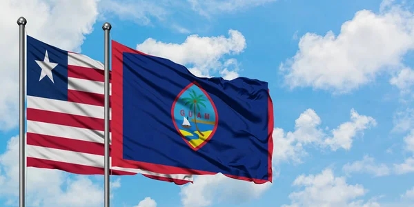 Liberia och Guam flagga vifta i vinden mot vit grumlig blå himmel tillsammans. Diplomatisk koncept, internationella relationer. — Stockfoto