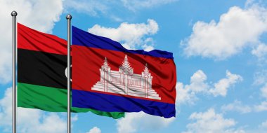 Libya ve Kamboçya bayrağı birlikte beyaz bulutlu mavi gökyüzüne karşı rüzgarsal sallayarak. Diplomasi kavramı, uluslararası ilişkiler.