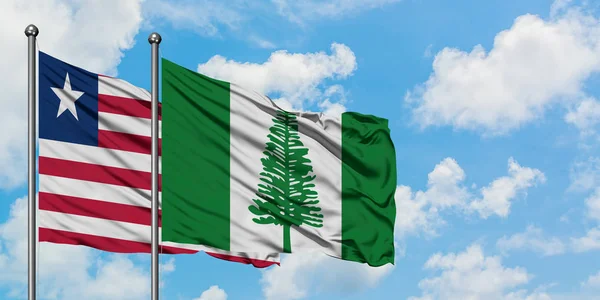 Libéria e Norfolk Island bandeira acenando no vento contra o céu azul nublado branco juntos. Conceito de diplomacia, relações internacionais . — Fotografia de Stock