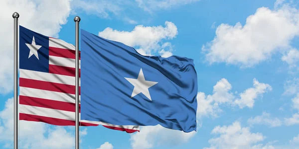 Liberia i Somalia flagi machając w wiatr przed białym zachmurzone błękitne niebo razem. Koncepcja dyplomacji, stosunki międzynarodowe. — Zdjęcie stockowe
