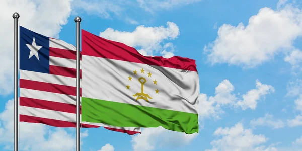 Bandera de Liberia y Tayikistán ondeando en el viento contra el cielo azul nublado blanco juntos. Concepto diplomático, relaciones internacionales . — Foto de Stock