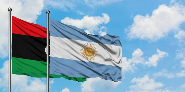 Bandera de Libia y Argentina ondeando en el viento contra el cielo azul nublado blanco juntos. Concepto diplomático, relaciones internacionales . — Foto de Stock