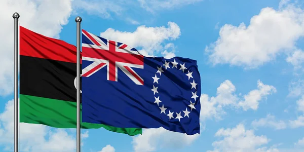 Bandera de Libia y las Islas Cook ondeando en el viento contra el cielo azul nublado blanco juntos. Concepto diplomático, relaciones internacionales . — Foto de Stock