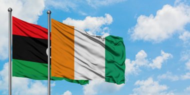 Libya ve Fildişi Sahili bayrağı birlikte beyaz bulutlu mavi gökyüzüne karşı rüzgarda sallayarak. Diplomasi kavramı, uluslararası ilişkiler.