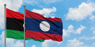 Libya ve Laos bayrağı birlikte beyaz bulutlu mavi gökyüzüne karşı rüzgarsal sallayarak. Diplomasi kavramı, uluslararası ilişkiler.