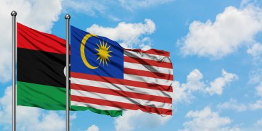 Libya ve Malezya bayrağı birlikte beyaz bulutlu mavi gökyüzüne karşı rüzgarsal sallayarak. Diplomasi kavramı, uluslararası ilişkiler.