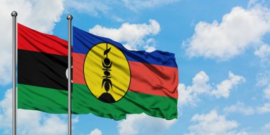 Libya ve Yeni Kaledonya bayrağı birlikte beyaz bulutlu mavi gökyüzüne karşı rüzgarda sallayarak. Diplomasi kavramı, uluslararası ilişkiler.