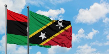 Libya ve Saint Kitts ve Nevis bayrağı birlikte beyaz bulutlu mavi gökyüzüne karşı rüzgarda sallayarak. Diplomasi kavramı, uluslararası ilişkiler.
