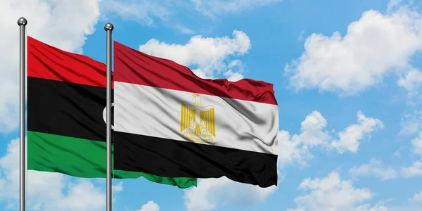 Bandera de Libia y Egipto ondeando en el viento contra el cielo azul nublado blanco juntos. Concepto diplomático, relaciones internacionales . — Foto de Stock