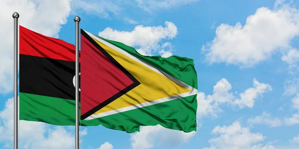 Libia e Guyana sventolano insieme la bandiera contro il bianco cielo azzurro nuvoloso. Concetto di diplomazia, relazioni internazionali . — Foto Stock