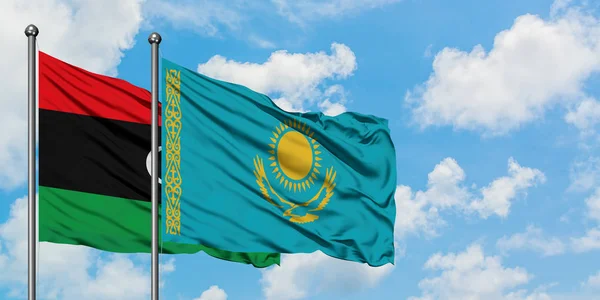 Bandera de Libia y Kazajstán ondeando en el viento contra el cielo azul nublado blanco juntos. Concepto diplomático, relaciones internacionales . — Foto de Stock