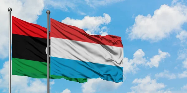 Bandera de Libia y Luxemburgo ondeando en el viento contra el cielo azul nublado blanco juntos. Concepto diplomático, relaciones internacionales . — Foto de Stock