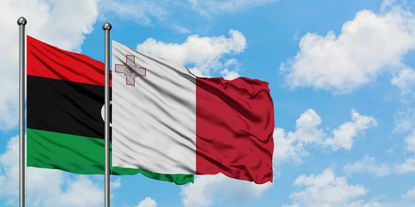 Bandera de Libia y Malta ondeando en el viento contra el cielo azul nublado blanco juntos. Concepto diplomático, relaciones internacionales . — Foto de Stock