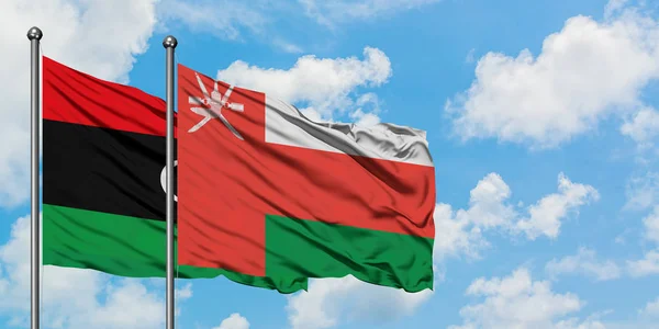 Bandera de Libia y Omán ondeando en el viento contra el cielo azul nublado blanco juntos. Concepto diplomático, relaciones internacionales . — Foto de Stock