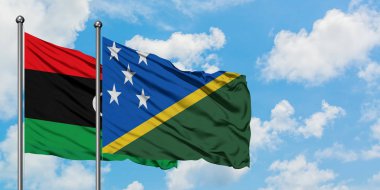 Libya ve Solomon Adaları bayrağı birlikte beyaz bulutlu mavi gökyüzüne karşı rüzgarsal sallayarak. Diplomasi kavramı, uluslararası ilişkiler.