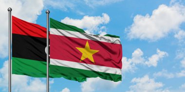 Libya ve Surinam bayrağı birlikte beyaz bulutlu mavi gökyüzüne karşı rüzgarsal sallayarak. Diplomasi kavramı, uluslararası ilişkiler.