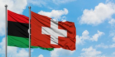 Libya ve İsviçre bayrağı birlikte beyaz bulutlu mavi gökyüzüne karşı rüzgarsal sallayarak. Diplomasi kavramı, uluslararası ilişkiler.