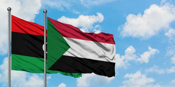 Bandera de Libia y Sudán ondeando en el viento contra el cielo azul nublado blanco juntos. Concepto diplomático, relaciones internacionales . — Foto de Stock