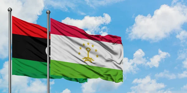 Bandera de Libia y Tayikistán ondeando en el viento contra el cielo azul nublado blanco juntos. Concepto diplomático, relaciones internacionales . — Foto de Stock