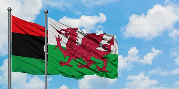 Líbia e País de Gales acenando com o vento contra o céu azul nublado branco juntos. Conceito de diplomacia, relações internacionais . — Fotografia de Stock
