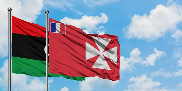 Libia y Wallis Y la bandera de Futuna ondeando en el viento contra el cielo azul nublado blanco juntos. Concepto diplomático, relaciones internacionales . — Foto de Stock