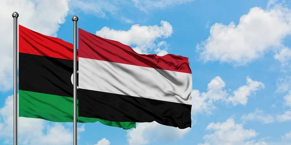 Bandera de Libia y Yemen ondeando en el viento contra el cielo azul nublado blanco juntos. Concepto diplomático, relaciones internacionales . — Foto de Stock