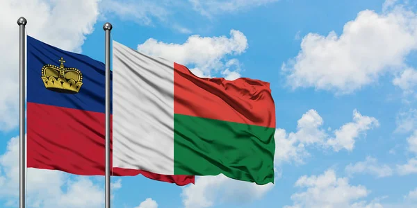 Bandera de Liechtenstein y Madagascar ondeando en el viento contra el cielo azul nublado blanco juntos. Concepto diplomático, relaciones internacionales . — Foto de Stock