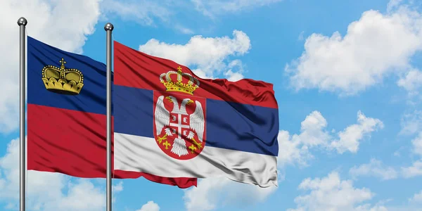 Bandera de Liechtenstein y Serbia ondeando en el viento contra el cielo azul nublado blanco juntos. Concepto diplomático, relaciones internacionales . — Foto de Stock