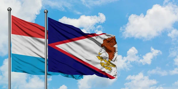 Bandera de Luxemburgo y Samoa Americana ondeando en el viento contra el cielo azul nublado blanco juntos. Concepto diplomático, relaciones internacionales . — Foto de Stock