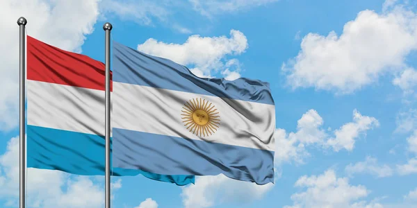Bandera de Luxemburgo y Argentina ondeando en el viento contra el cielo azul nublado blanco juntos. Concepto diplomático, relaciones internacionales . — Foto de Stock
