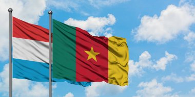 Lüksemburg ve Kamerun bayrağı birlikte beyaz bulutlu mavi gökyüzüne karşı rüzgarsal sallayarak. Diplomasi kavramı, uluslararası ilişkiler.