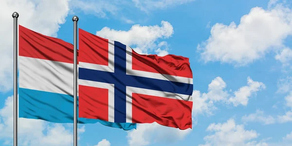 Bandera de Luxemburgo y Bouvet Islands ondeando en el viento contra el cielo azul nublado blanco juntos. Concepto diplomático, relaciones internacionales . — Foto de Stock