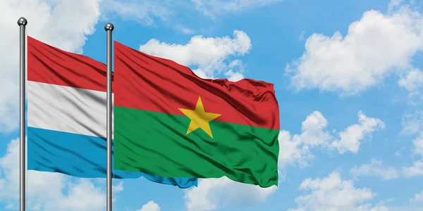 Bandera de Luxemburgo y Burkina Faso ondeando en el viento contra el cielo azul nublado blanco juntos. Concepto diplomático, relaciones internacionales . — Foto de Stock