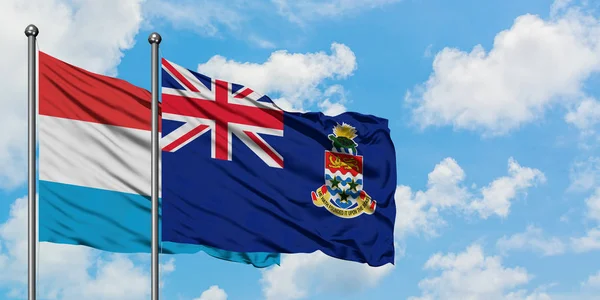 Bandera de Luxemburgo y las Islas Caimán ondeando en el viento contra el cielo azul nublado blanco juntos. Concepto diplomático, relaciones internacionales . — Foto de Stock
