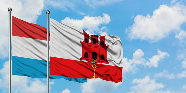 A bandeira de Luxemburgo e Gibraltar agitando no vento contra o céu azul nublado branco juntos. Conceito de diplomacia, relações internacionais . — Fotografia de Stock