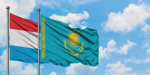 Bandera de Luxemburgo y Kazajstán ondeando en el viento contra el cielo azul nublado blanco juntos. Concepto diplomático, relaciones internacionales . — Foto de Stock