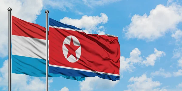 Bandera de Luxemburgo y Corea del Norte ondeando en el viento contra el cielo azul nublado blanco juntos. Concepto diplomático, relaciones internacionales . — Foto de Stock