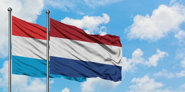 Drapeau luxembourgeois et néerlandais agitant dans le vent contre ciel bleu nuageux blanc ensemble. Concept de diplomatie, relations internationales . — Photo