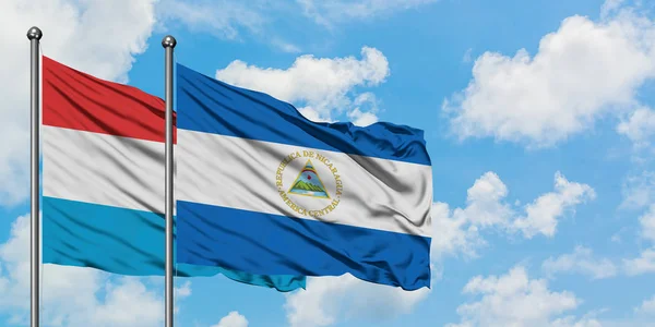 Bandera de Luxemburgo y Nicaragua ondeando en el viento contra el cielo azul nublado blanco juntos. Concepto diplomático, relaciones internacionales . — Foto de Stock