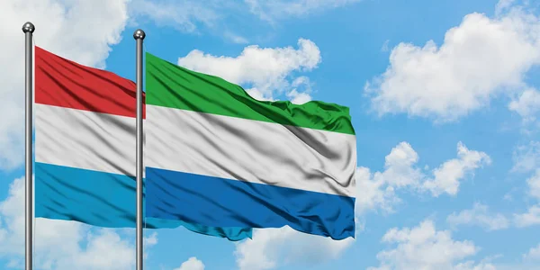 Lussemburgo e Sierra Leone sventolano insieme la bandiera contro il bianco cielo azzurro nuvoloso. Concetto di diplomazia, relazioni internazionali . — Foto Stock