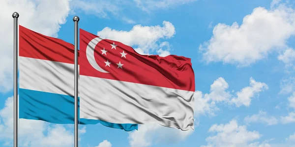 A bandeira de Luxemburgo e Singapura agitando no vento contra o céu azul nublado branco juntos. Conceito de diplomacia, relações internacionais . — Fotografia de Stock
