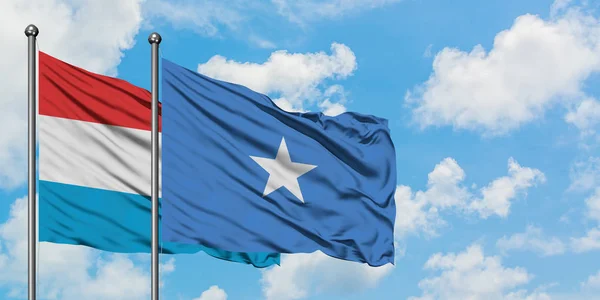 Lussemburgo e Somalia sventolano insieme la bandiera contro il bianco cielo azzurro nuvoloso. Concetto di diplomazia, relazioni internazionali . — Foto Stock